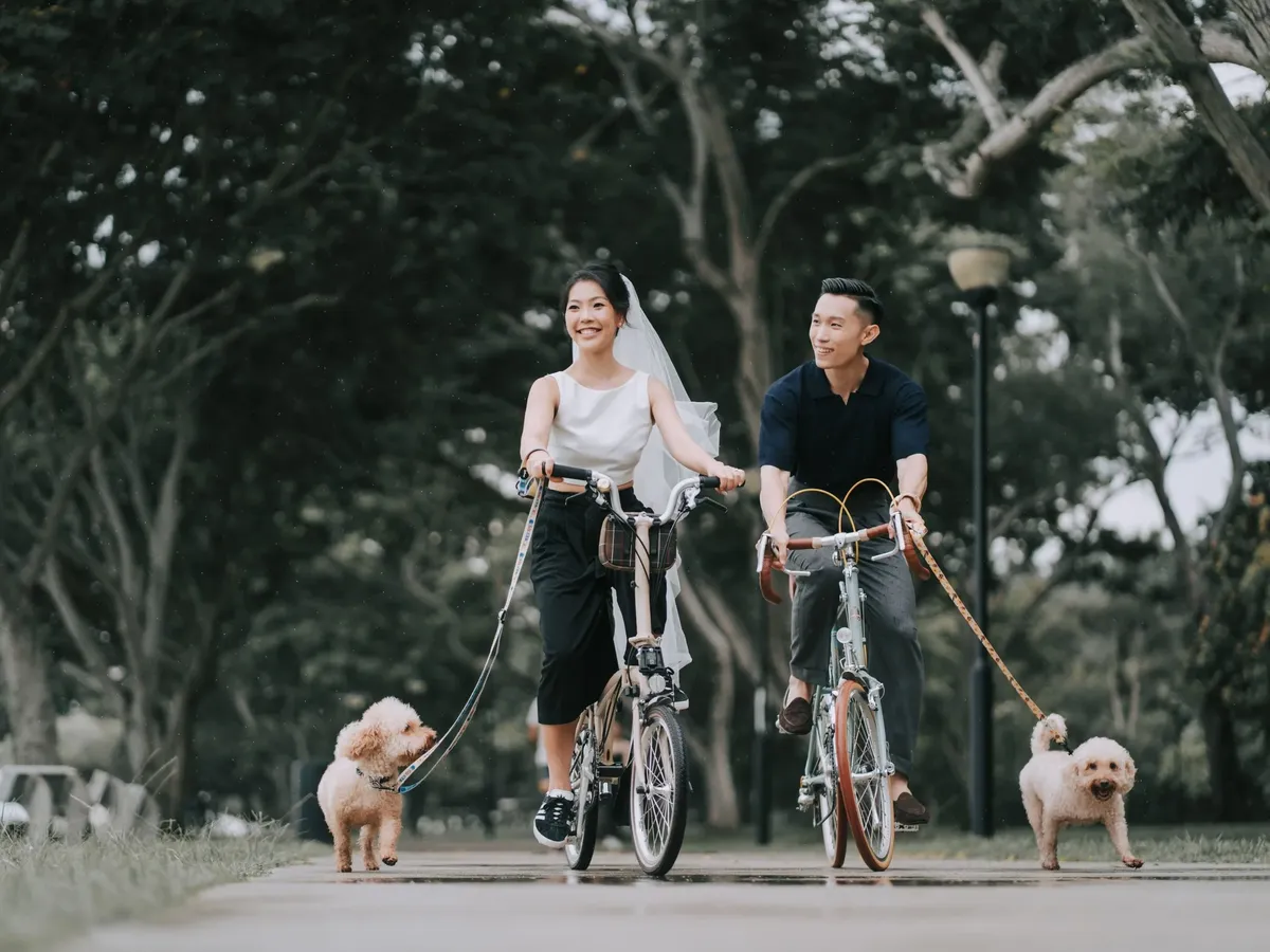 Claire cycling through a park with her partner and their two poodles